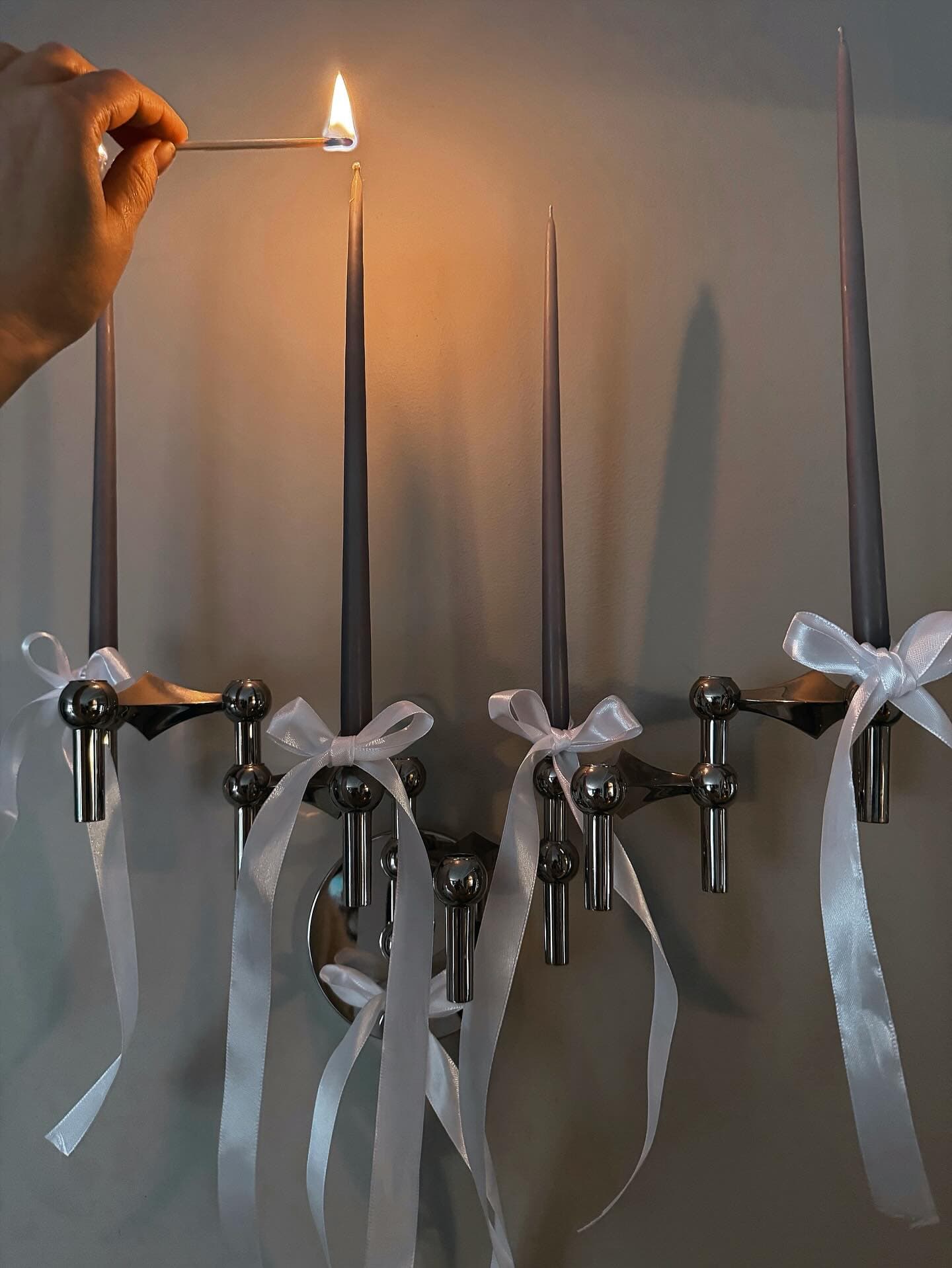 Hand lights tall candles in a candelabra with white ribbon.